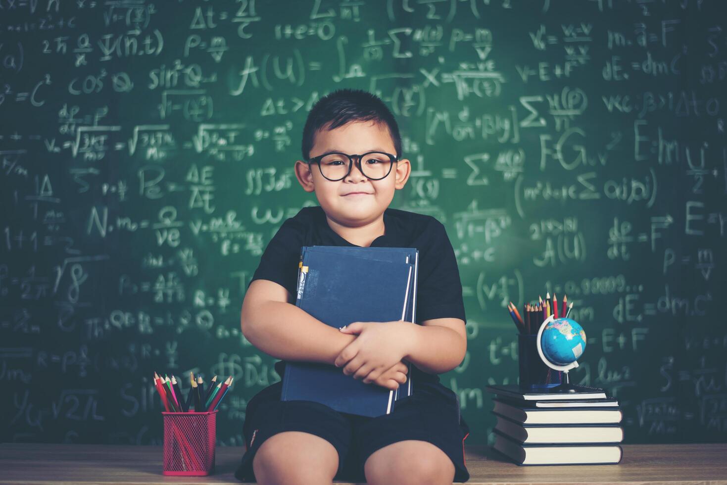 jongen met boeken zitten in de buurt van groen schoolbord foto