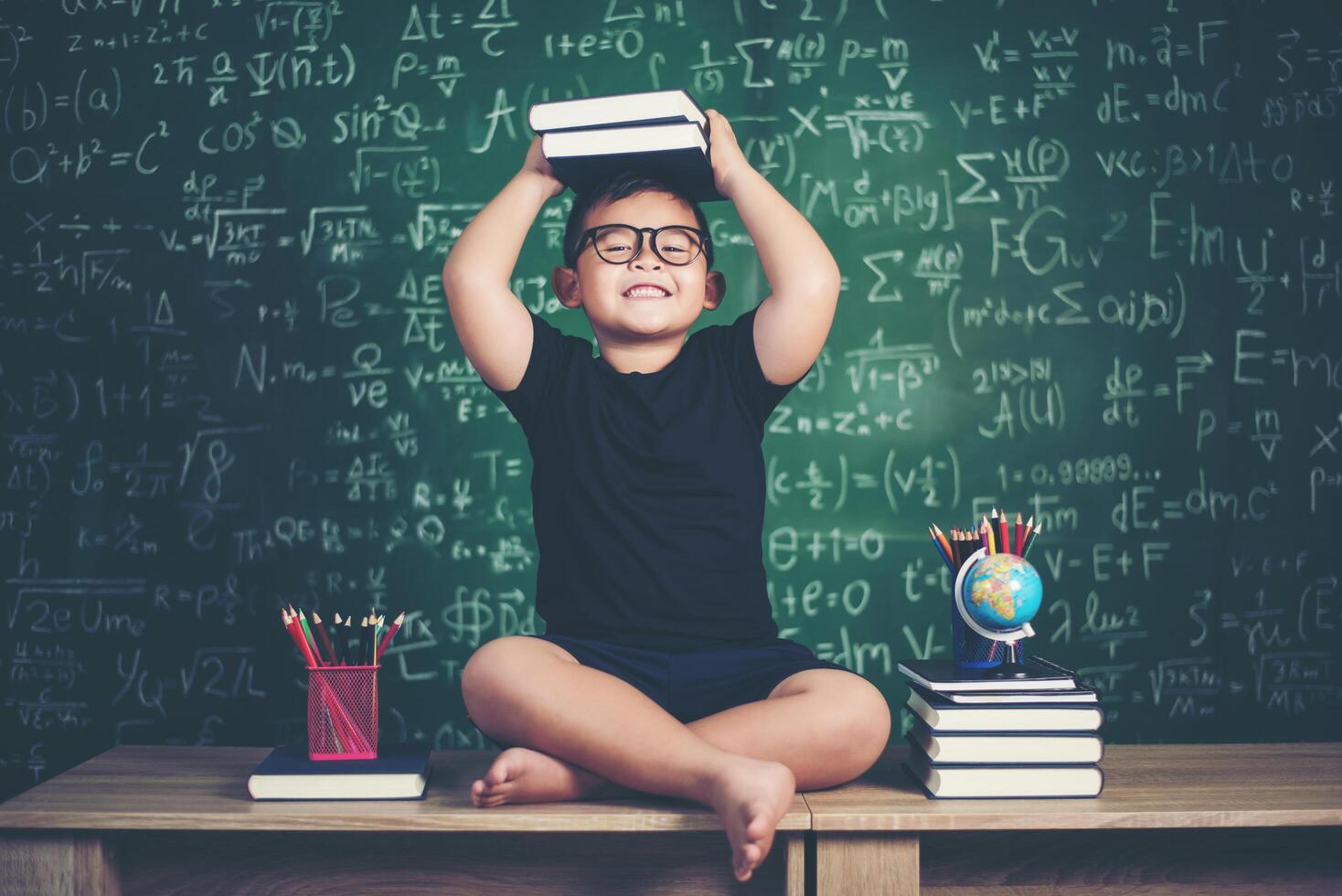 jongen met boeken zitten in de buurt van groen schoolbord foto