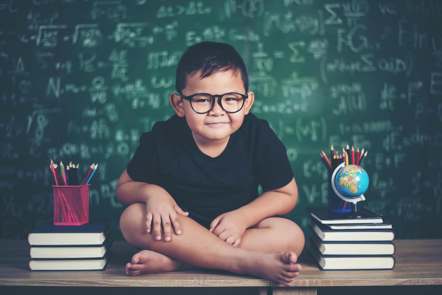 nadenkende kleine jongen met boek in de buurt van een schoolbestuur foto