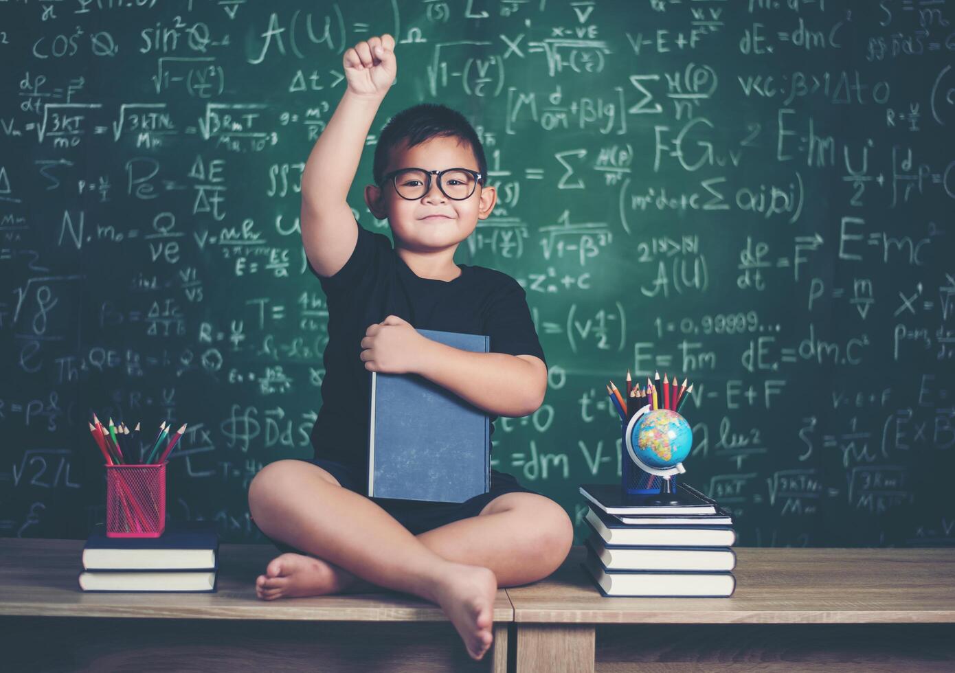 jongen met boeken zitten in de buurt van groen schoolbord foto