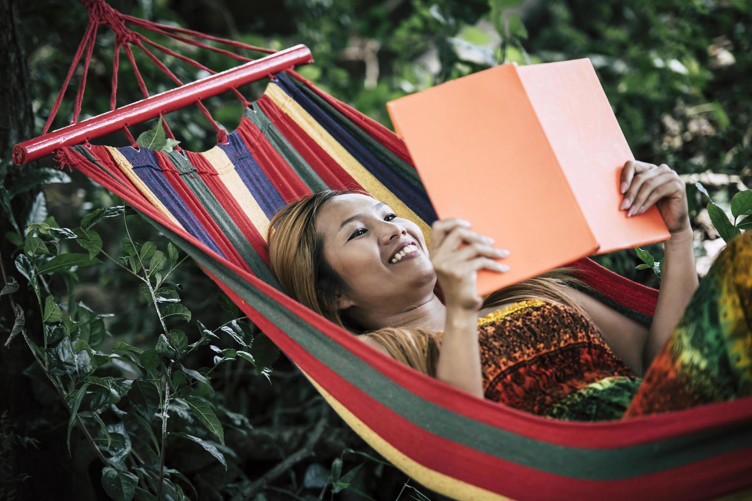 jonge vrouw die een boek leest dat in een hangmat ligt foto