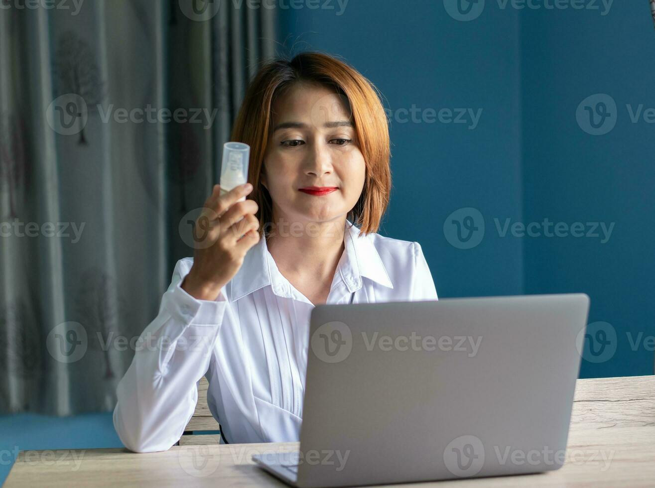 Aziatisch vrouw zittend Aan stoel Holding geneeskunde fles en gebruik makend van tablet naar zoeken voorschrift Aan geneeskunde informatie online foto