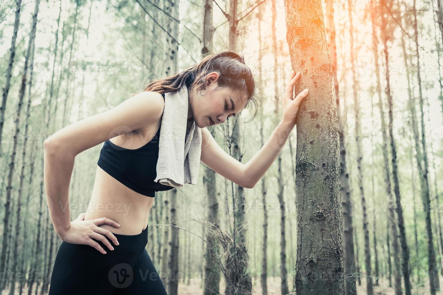 Aziatische schoonheidsvrouw die moe is van joggen in het bos foto