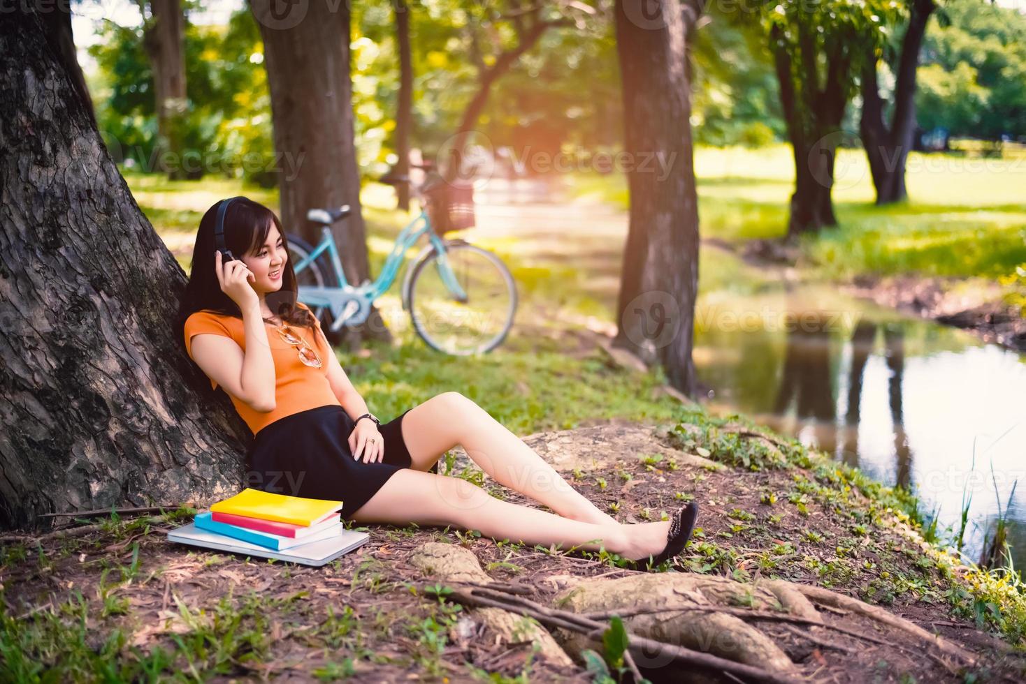 vrouw ontspannen onder de boom in het park met koptelefoon foto