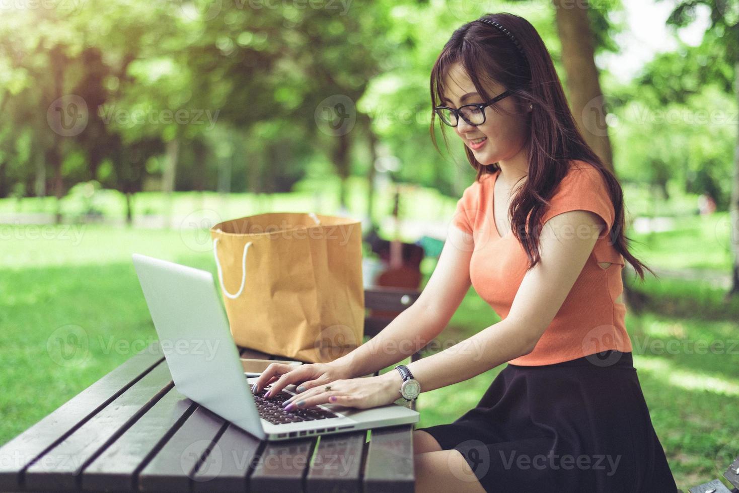 Aziatische vrouw die op laptoptoetsenbord in openluchtpark gebruikt en typt foto