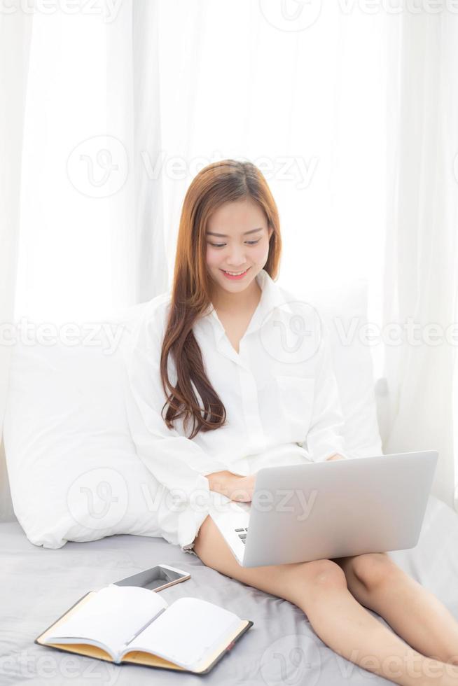 jonge Aziatische vrouw zittend op bed met behulp van laptopcomputer. foto