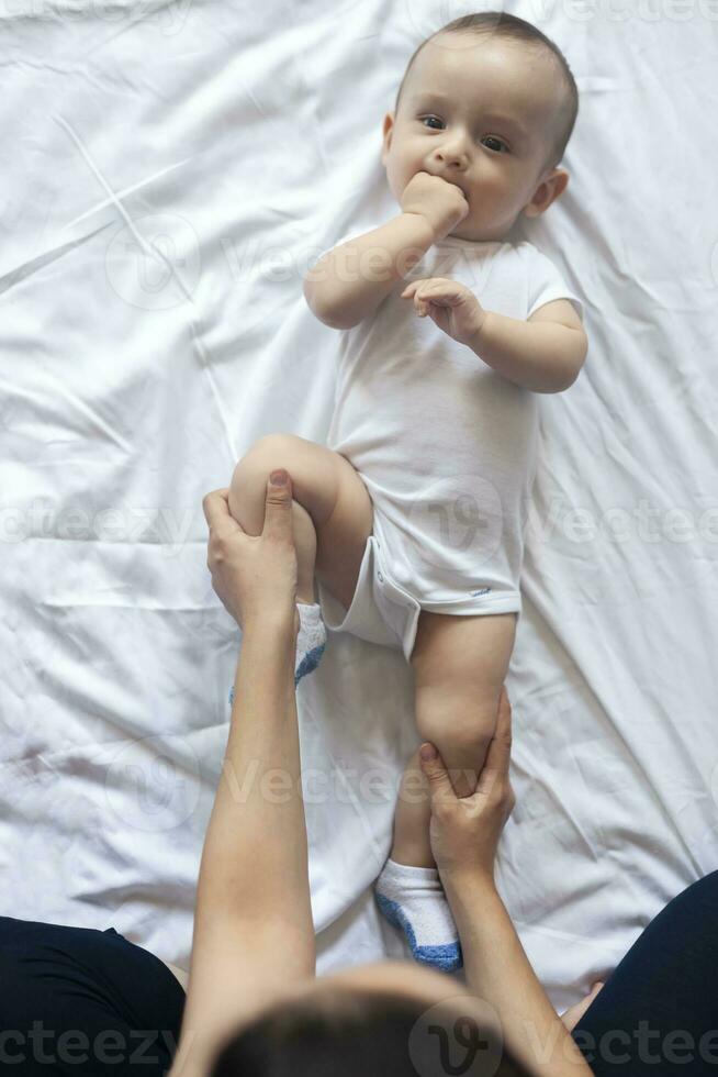 baby massage. mam aan het doen gymnastiek met kind. mama masseren schattig baby jongen. in beweging baby's poten naar helpen verlichten constipatie. jong moeder aan het doen opdrachten en bewegingen naar stimuleren baby's darmen. foto