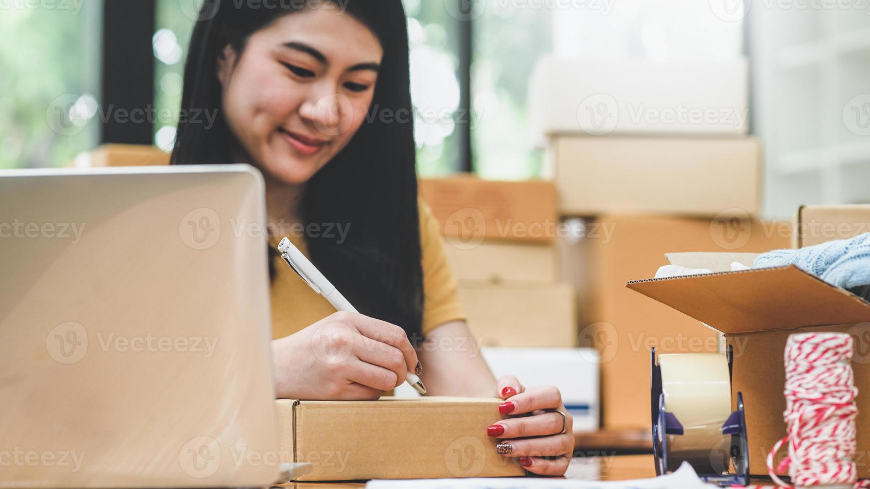 vrouw schrijft een adres op een pakketdoos voor levering aan een klant. foto