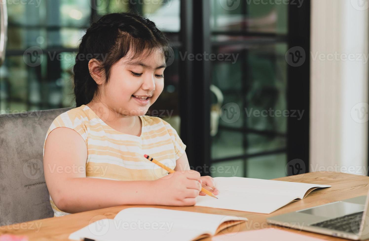 een Aziatisch kindmeisje in een goed humeur studeert thuis. foto