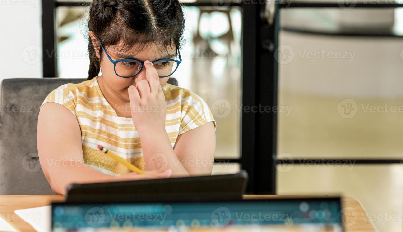 aziatisch kindmeisje legt de hand op een bril en ziet er moe uit van het studeren. foto