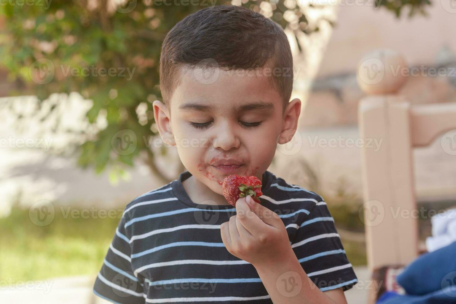 een weinig jongen aan het eten aardbeien. zomer voedsel. een jong kind eet een lekker aardbei in heet zomer dag foto