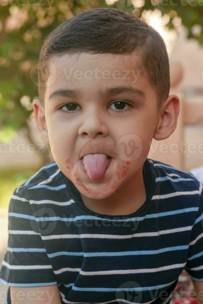 weinig jongen verdraait zijn gezicht Bij buitenshuis. 6 jaren oud kind in zomer vakantie. schattig weinig jongen voor de gek houden in de omgeving van. mensen, kinderjaren levensstijl concept. portret van jong kind maken grappig gezichten foto