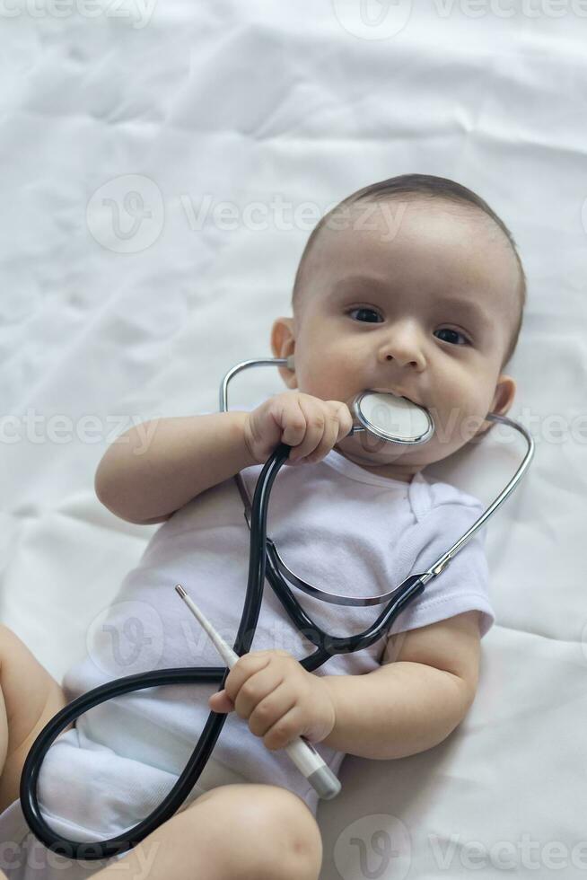 weinig schattig baby dokter. 6 maanden oud baby jongen spelen met stethoscoop. kind hebben pret Leuk vinden een dokter foto