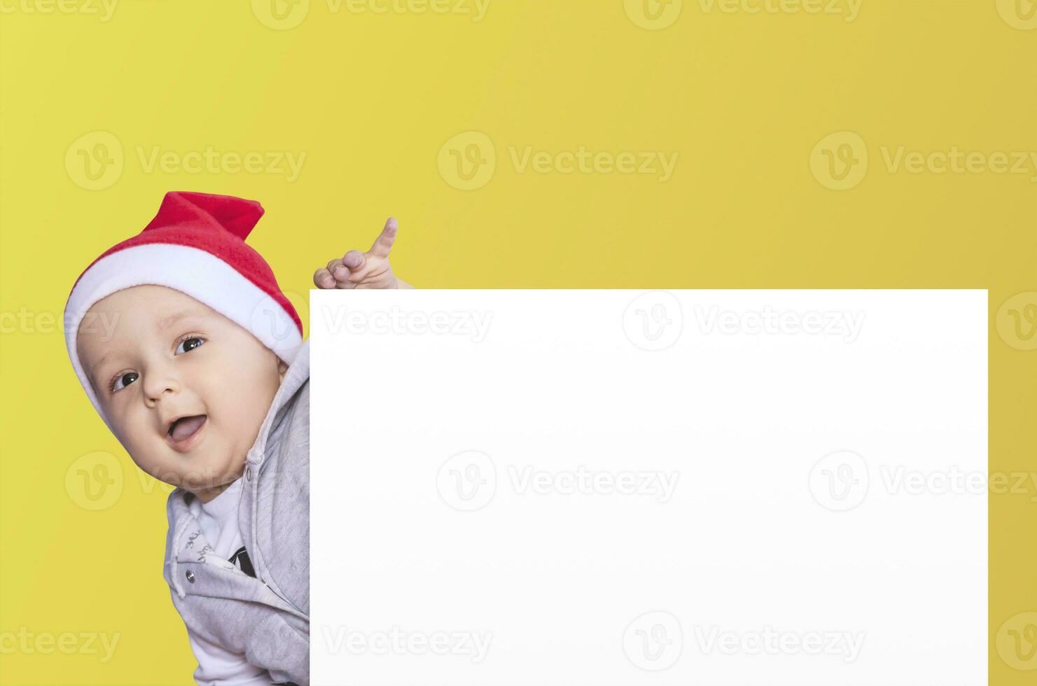 een weinig jongen met de kerstman pet Holding de blanco papier. de kerstman baby jongen met een leeg wit kaart. kopiëren ruimte voor uw reclame en tekst foto