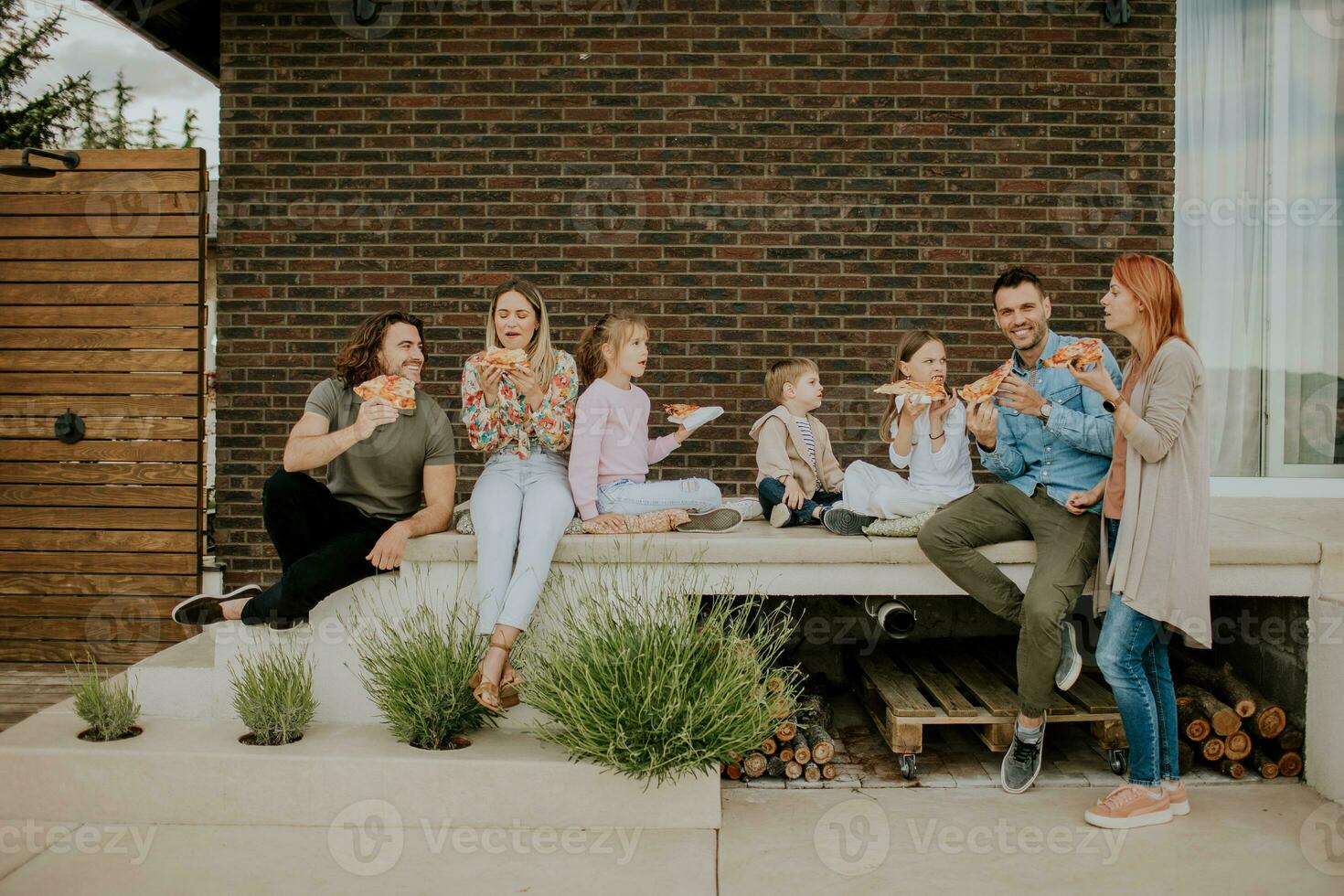 groep van jong mensen en kinderen aan het eten pizza in de huis achtertuin foto