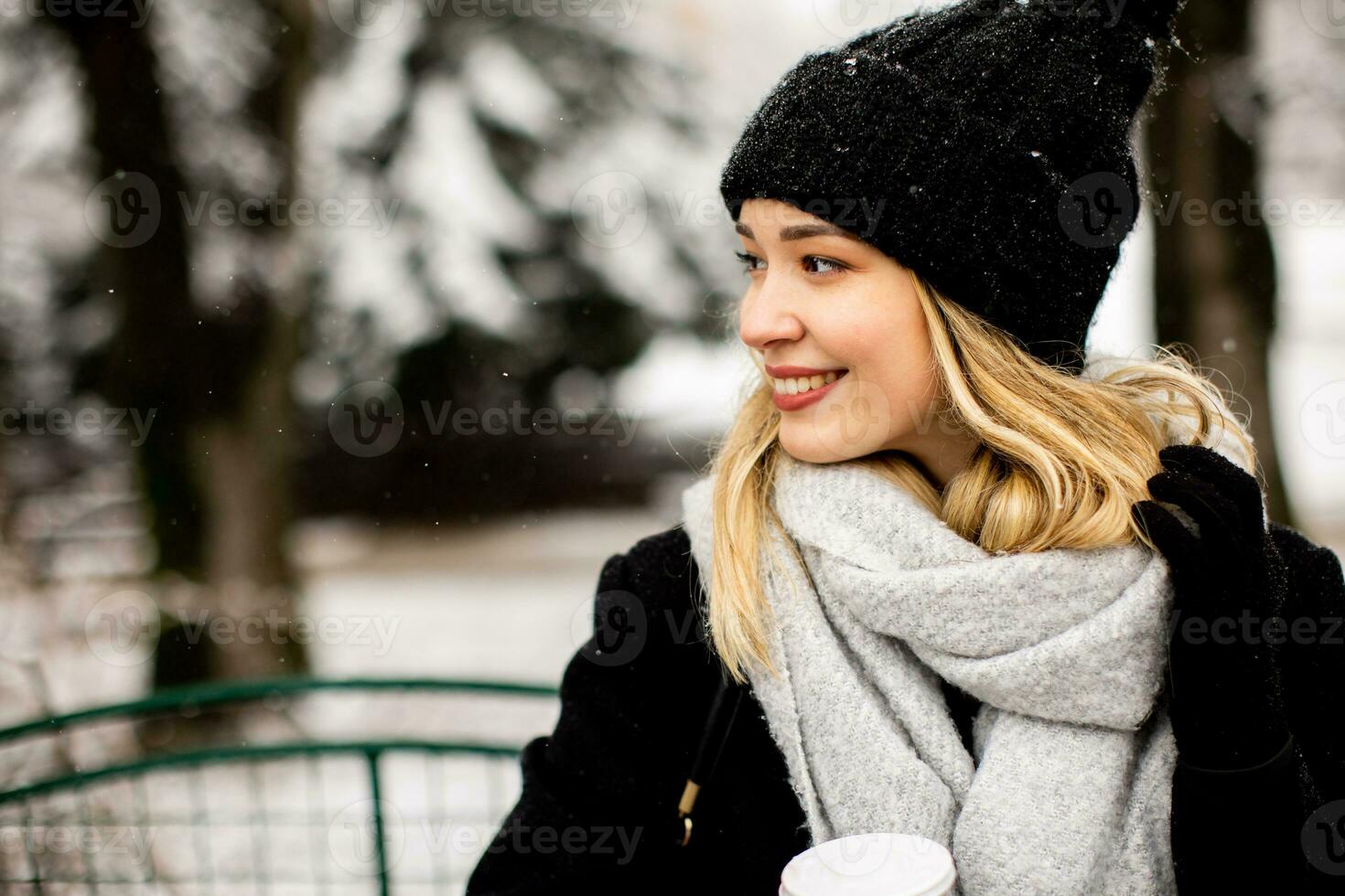 jong vrouw n warm kleren genieten van in sneeuw met meenemen koffie kop foto