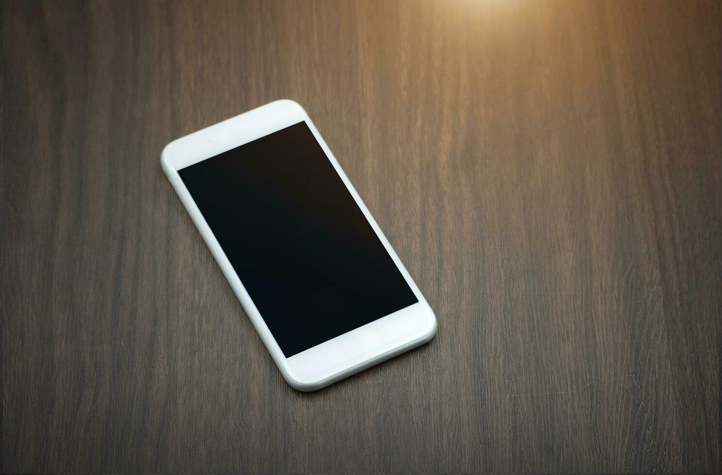 slim telefoon met blanco scherm aan het liegen Aan houten tafel foto
