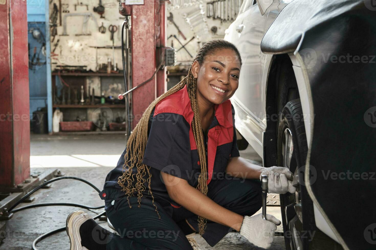 zwart vrouw automotive monteur arbeider schroeven auto wiel noten met moersleutel voor reparatie Bij garage, voertuig onderhoud onderhoud banen, industrie bezetting bedrijf, gelukkig arbeid werken, glimlach en vrolijk. foto