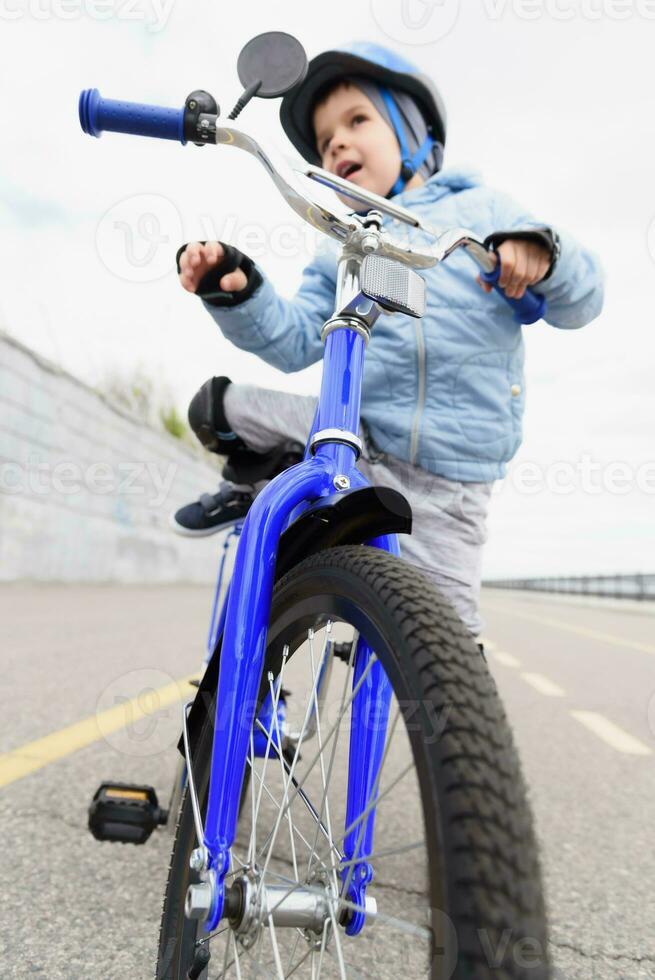 een kind in een helm en bescherming in een fiets rijden Aan natuur in de voorjaar foto