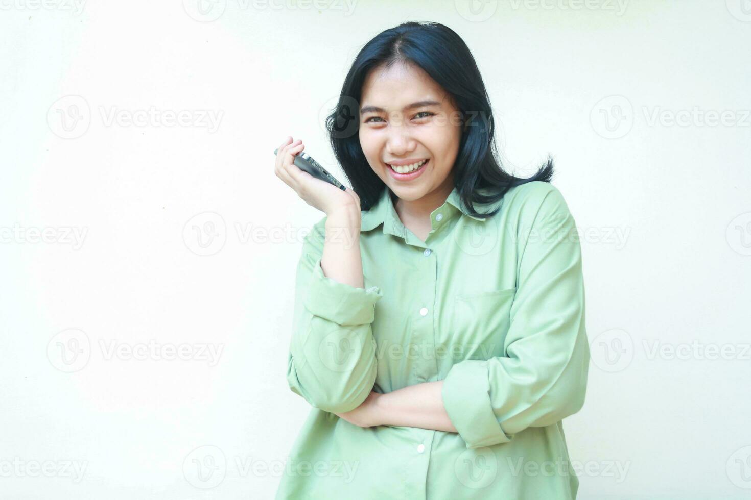 zorgeloos Aziatisch vrouw met donker haar- vervelend groen over- grootte overhemd genieten pratend Aan smartphone met armen gevouwen, speels elegant vrouw op zoek Bij camera, staand over- geïsoleerd wit achtergrond foto