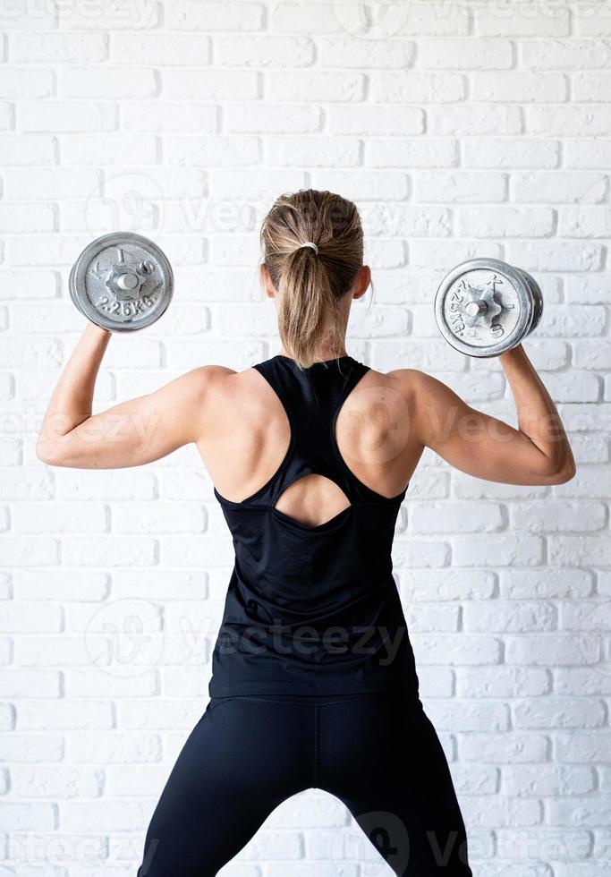 vrouw die haar rug- en armspieren laat trainen met een dumbbell foto