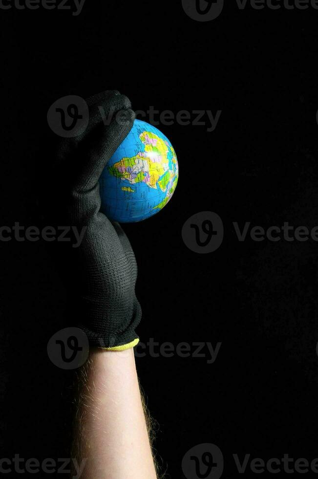 een persoon vervelend zwart handschoenen Holding omhoog een klein wereldbol foto