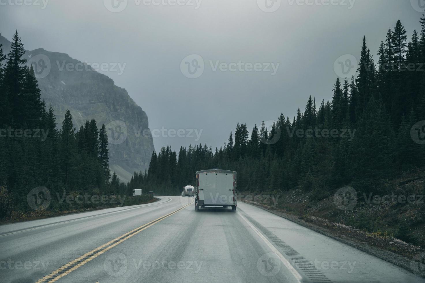 roadtrip met auto rijden in dennenbos met rotsachtige bergen op somber in Banff National Park foto