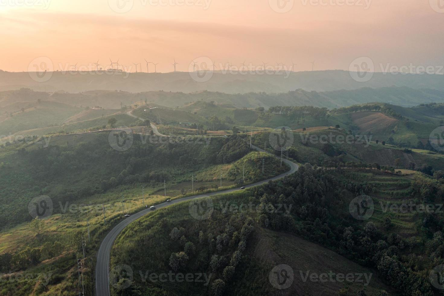 luchtfoto van gebogen snelweg op groene heuvel en windturbine op piek bij zonsondergang op het platteland foto