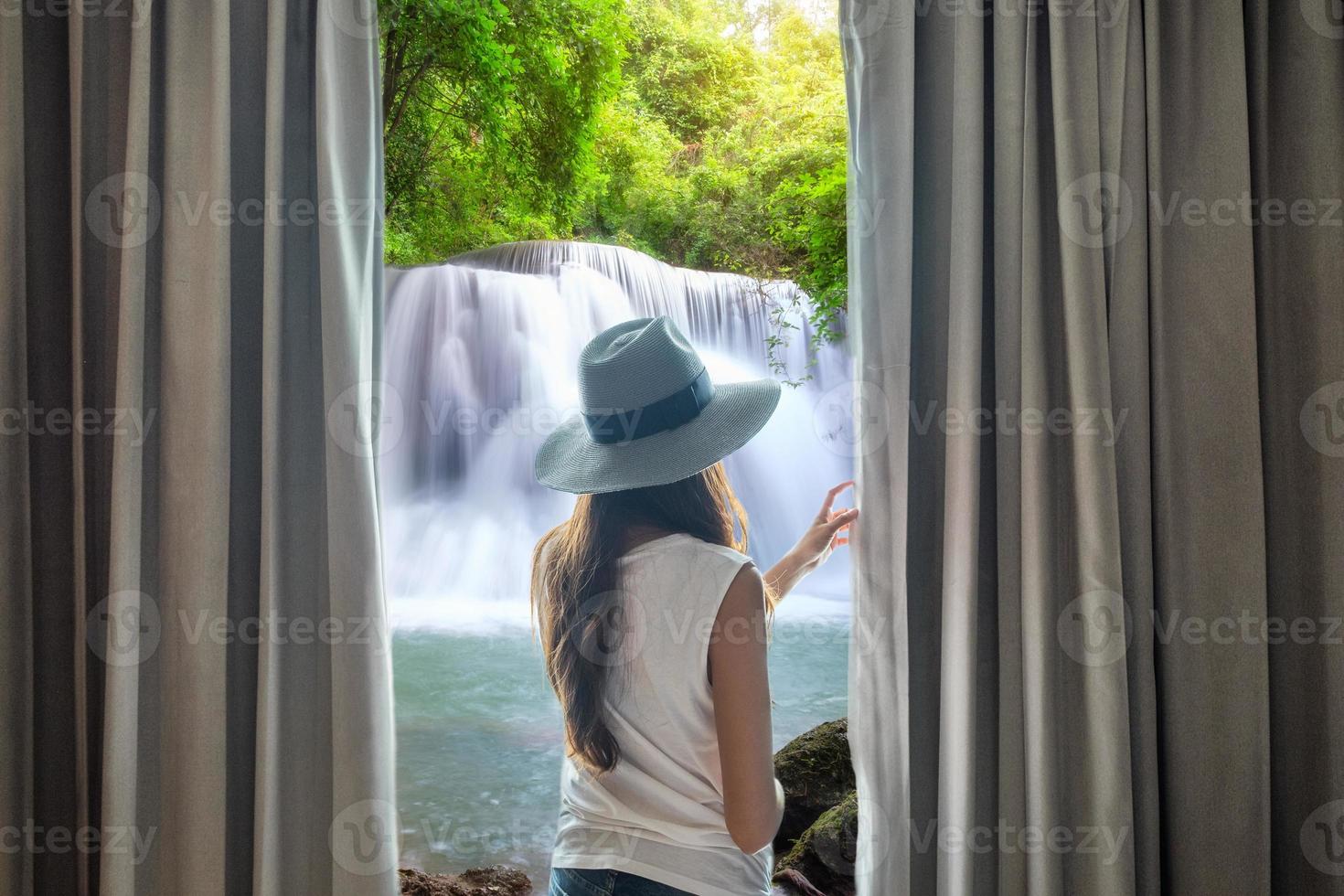 vrouw open gordijn om prachtige waterval te zien stromen natuurlijk foto