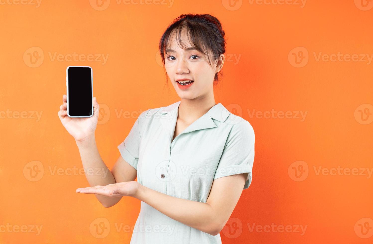 portret van een jong meisje dat het telefoonscherm toont, geïsoleerd op een oranje achtergrond foto
