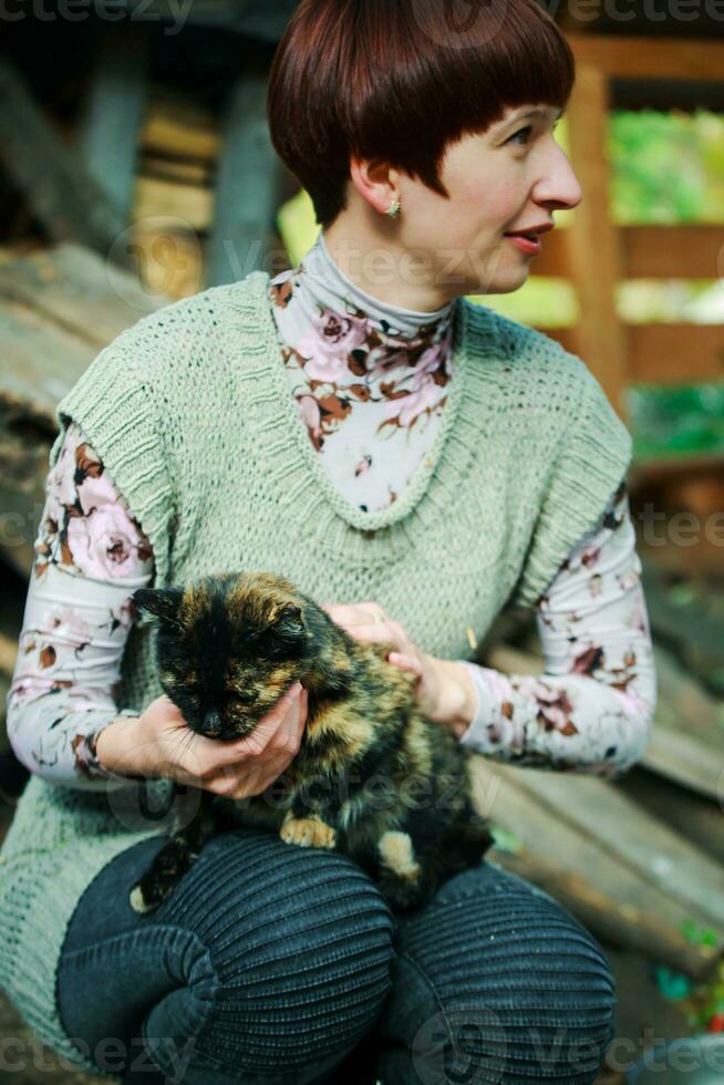 een vrouw is Holding een grijs dakloos katje in haar armen. de katje looks Bij de vrouw wie opgeslagen hem trouw. nemen de dier van de schuilplaats. foto