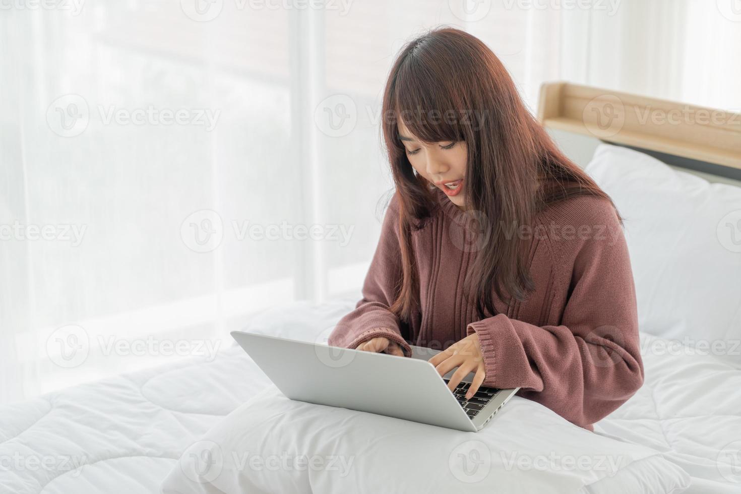 Aziatische vrouwen die met laptop op bed werken foto