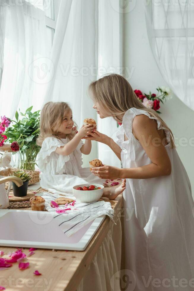 een weinig blond meisje met haar mam Aan een keuken aanrecht versierd met pioenrozen. de concept van de verhouding tussen moeder en dochter. voorjaar atmosfeer. foto