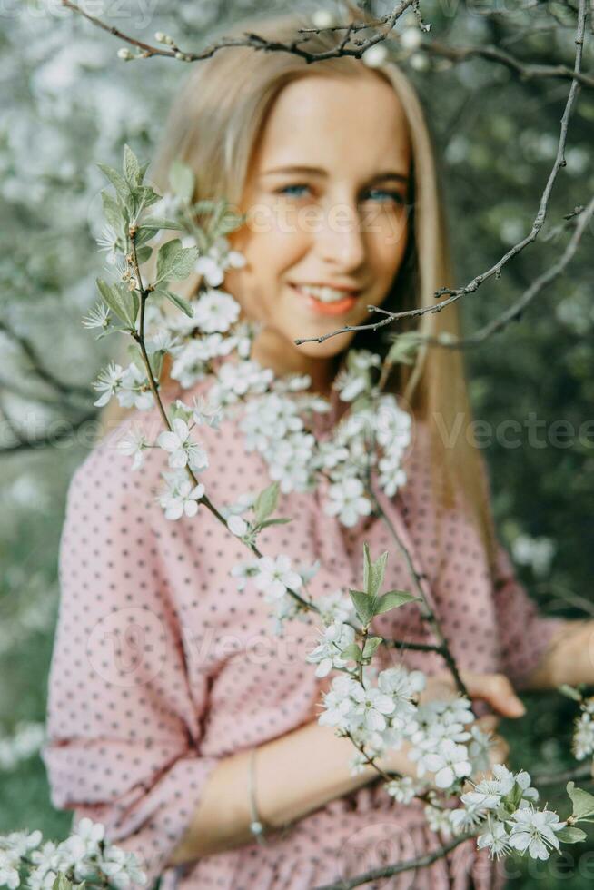 blond meisje Aan een voorjaar wandelen in de tuin met kers bloeit. vrouw portret, detailopname. een meisje in een roze polka punt jurk. foto