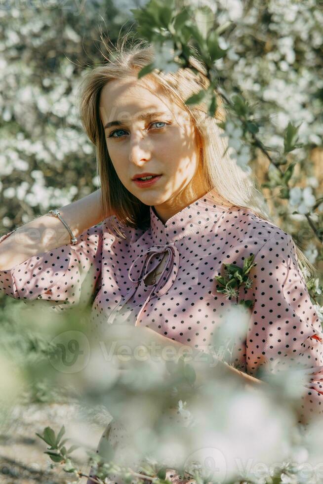 blond meisje Aan een voorjaar wandelen in de tuin met kers bloeit. vrouw portret, detailopname. een meisje in een roze polka punt jurk. foto