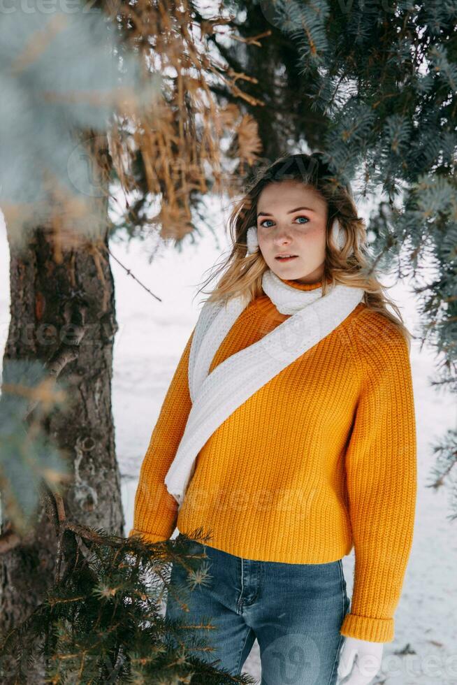 tiener blond in een geel trui buiten in winter. een tiener- meisje Aan een wandelen in winter kleren in een besneeuwd Woud foto