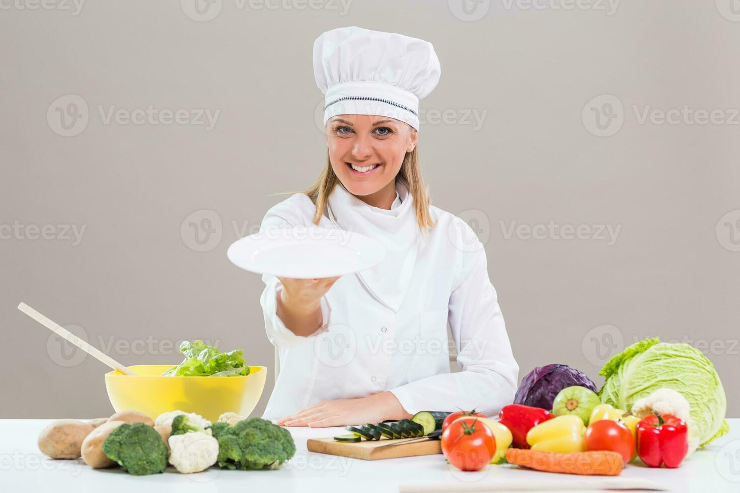 portret van vrolijk vrouw chef zittend Bij de tafel en tonen leeg bord terwijl maken gezond maaltijd. foto