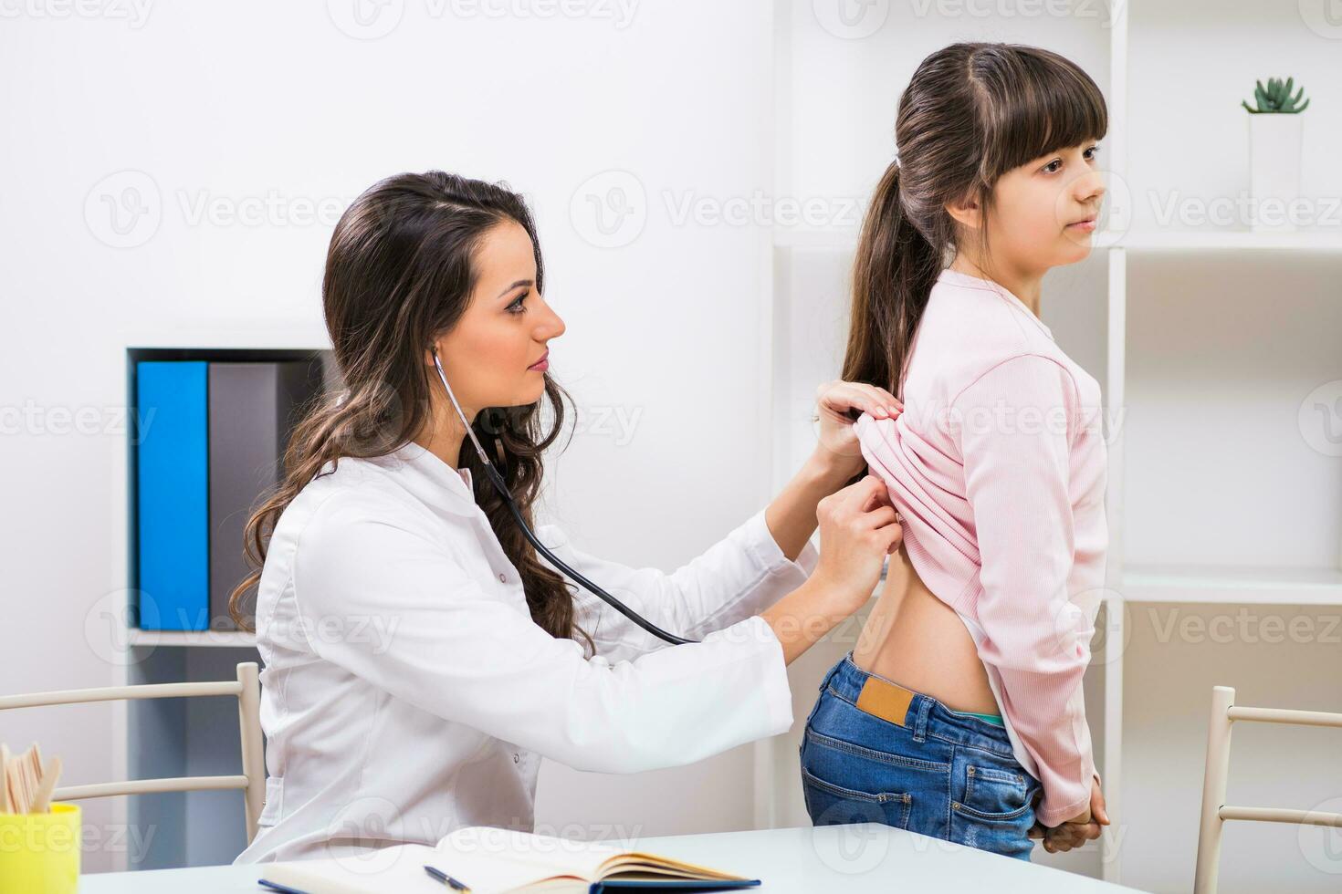 vrouw dokter luisteren longen van een weinig meisje met stethoscoop Bij medisch kantoor foto