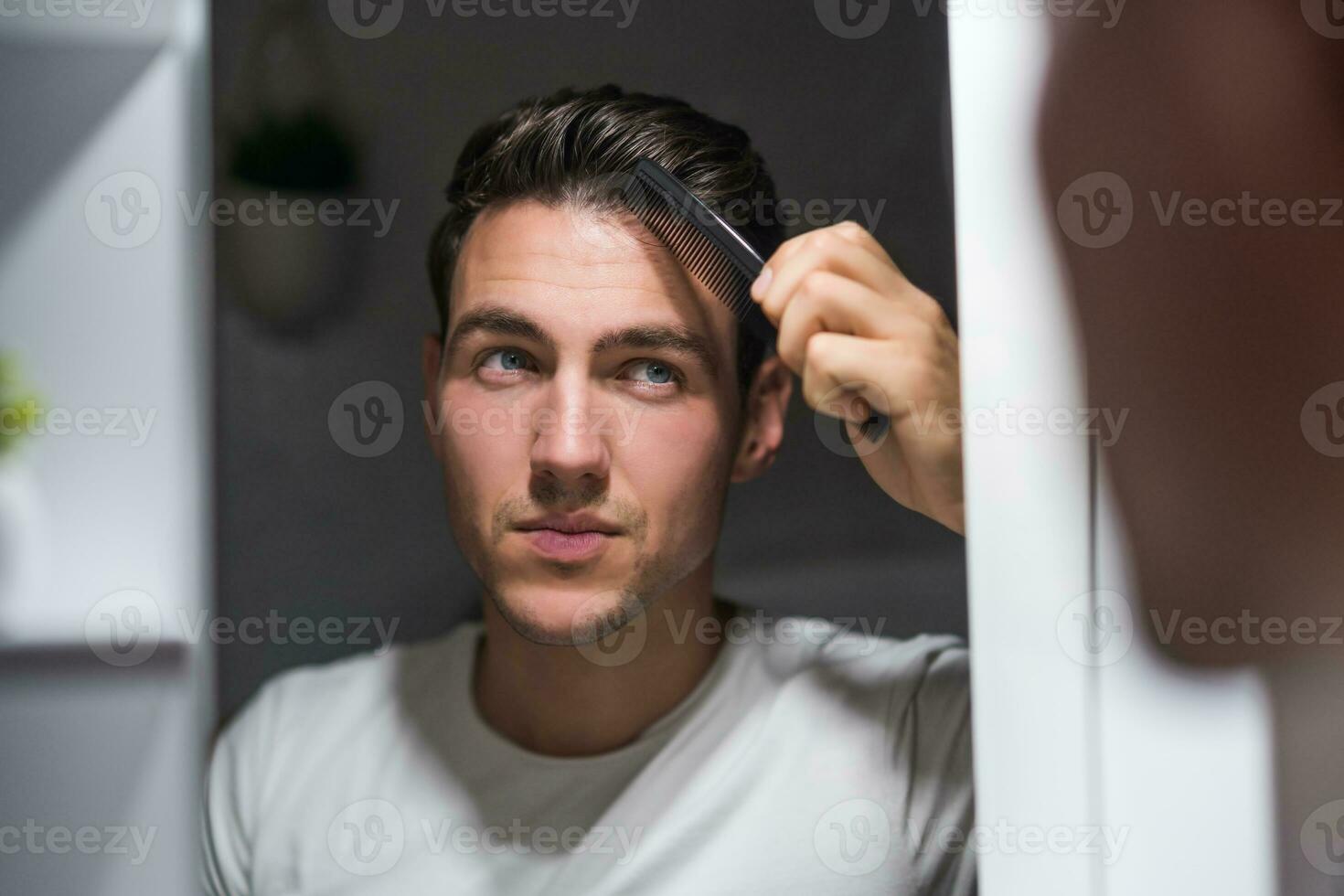 Mens kammen zijn haar- terwijl op zoek zichzelf in de spiegel foto