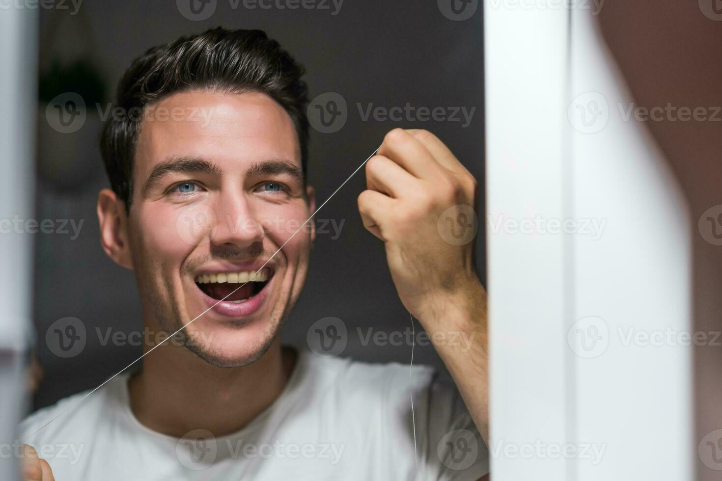Mens is gebruik makend van tandheelkundig floss terwijl op zoek zichzelf in de spiegel foto