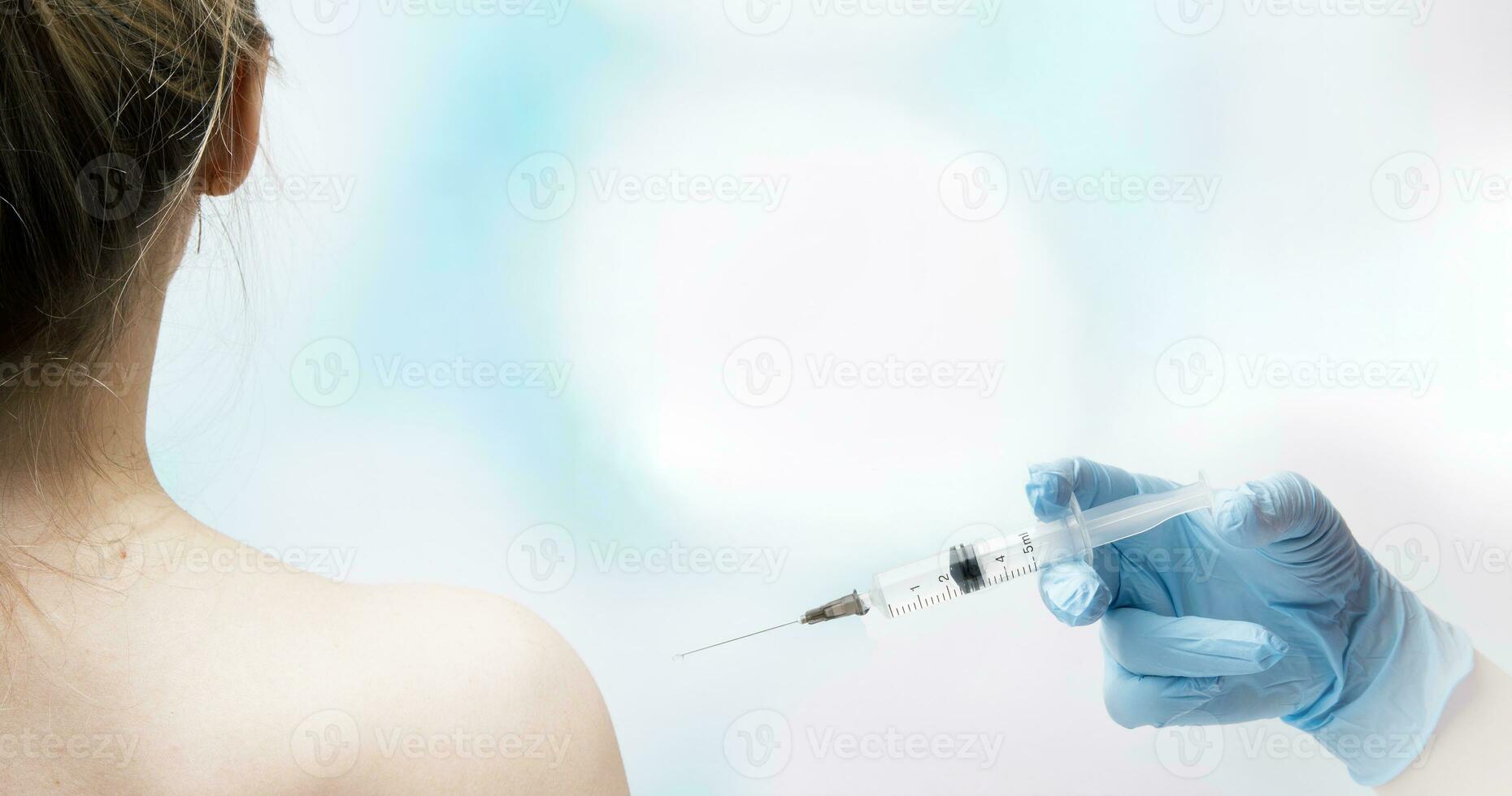 hand- van een medisch arbeider met een injectie injectiespuit bereidt zich voor naar worden gevaccineerd in de schouder van een jong vrouw foto