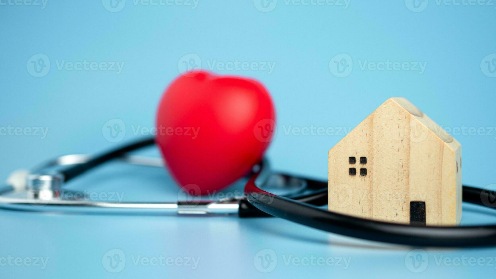 concept van Gezondheid verzekering en medisch welzijn, klein houten huis en rood hart met stethoscoop Aan blauw achtergrond, Gezondheid verzekering en toegang naar gezondheidszorg. foto