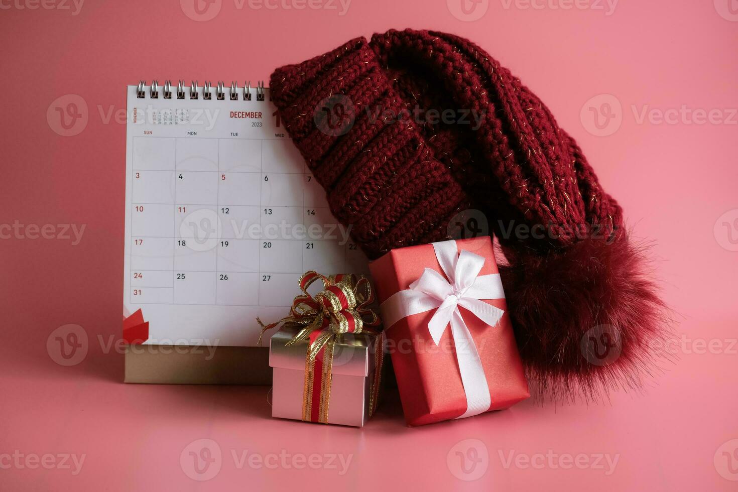 geschenk doos en kalender met een rood gebreid wol hoed Aan roze achtergrond. kerstmis dag concept. planning het roosteren agenda, evenement, organisator Kerstmis dag. foto