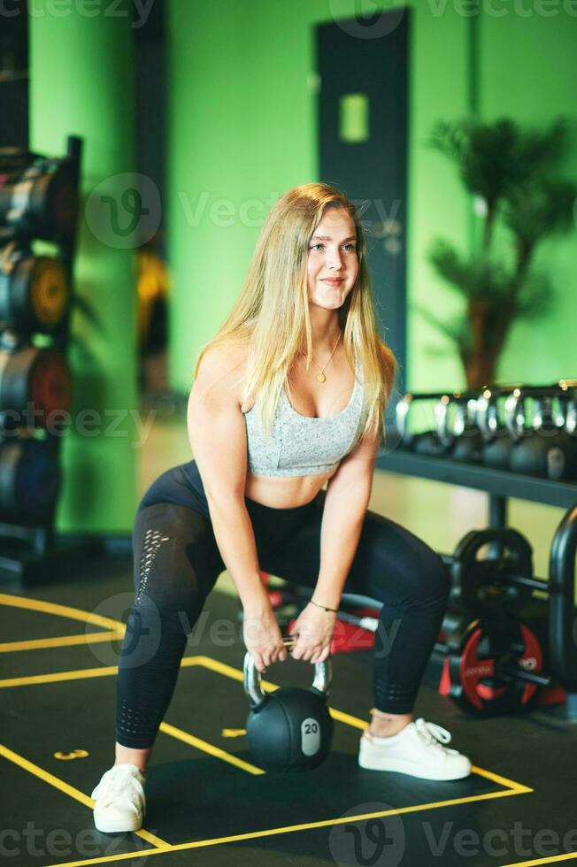 sportief vrouw aan het doen gehurkt sit-up oefening met 20 kg kettlebell foto