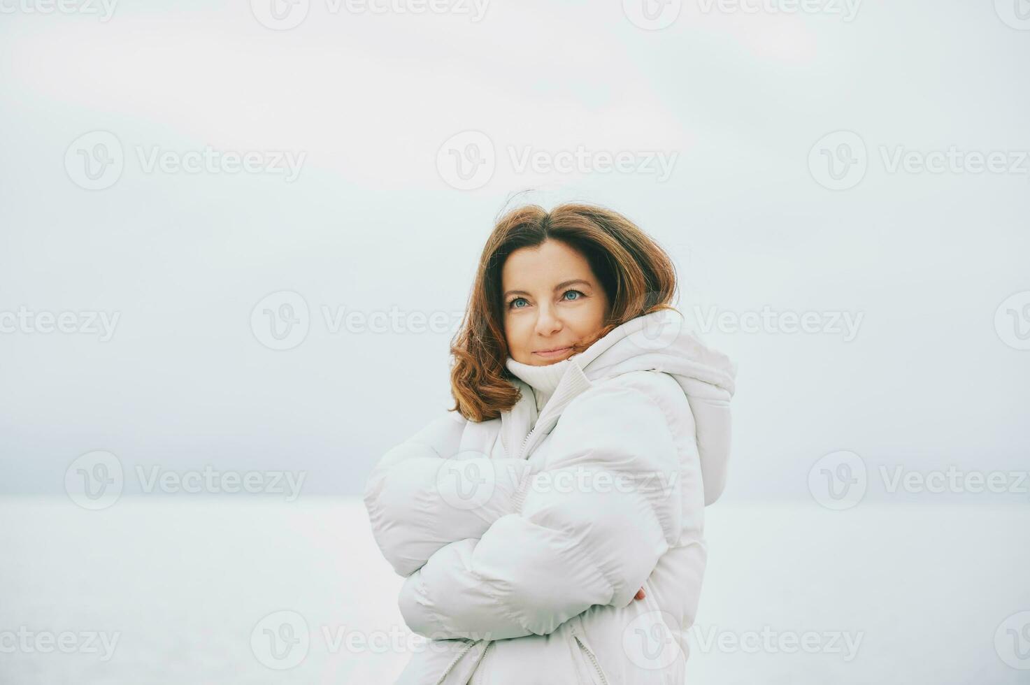 buitenshuis portret van mooi vrouw vervelend wit jasje, ontspannende De volgende naar meer of zee foto