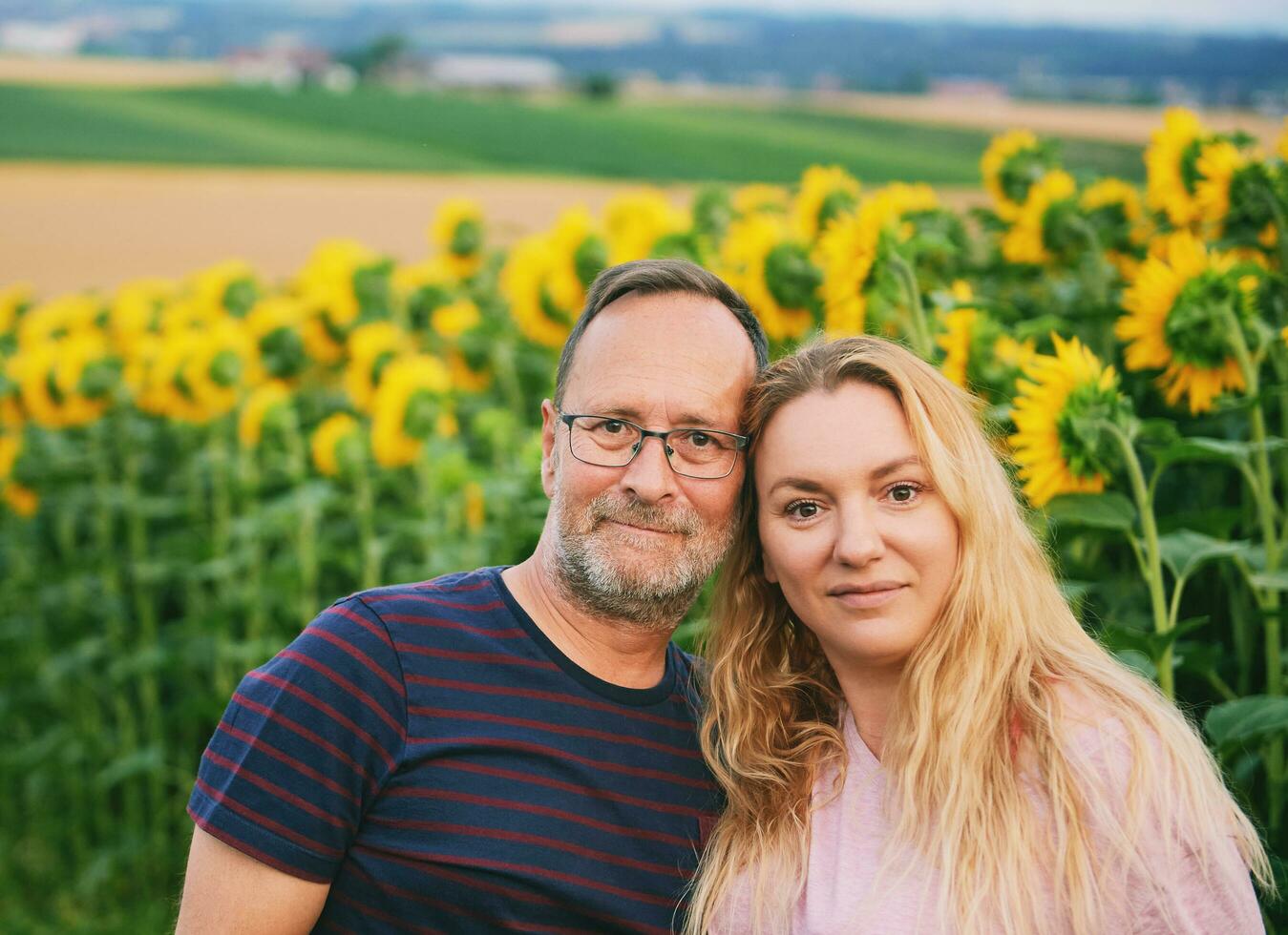 buitenshuis portret van midden- leeftijd paar genieten van mooi hoor dag in platteland, poseren De volgende naar zonnebloem veld- foto