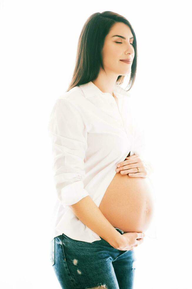 achtergrondverlichting portret van jong zwanger vrouw, vervelend wit overhemd en jeans foto