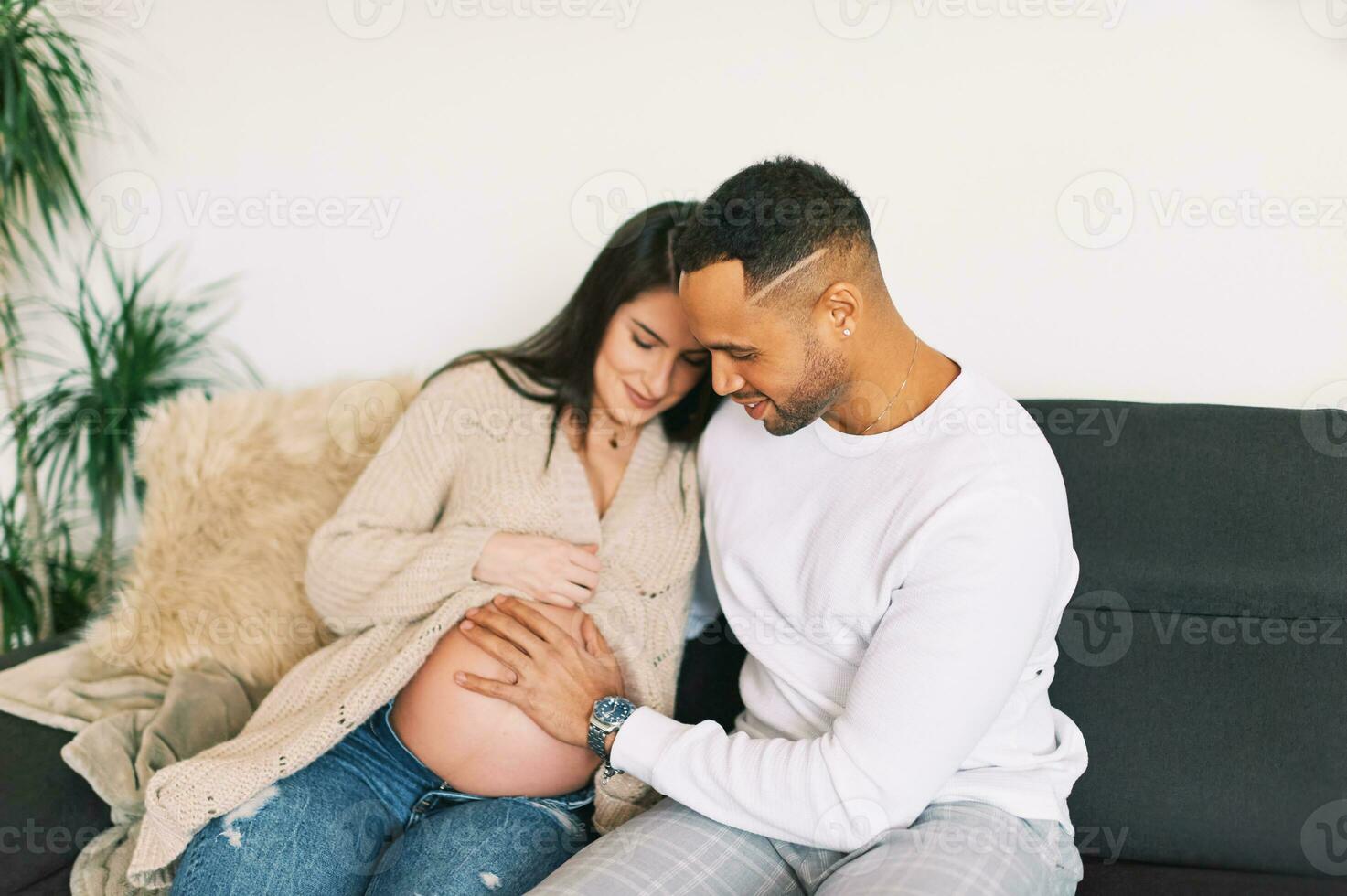 binnen- portret van gelukkig jong stel, zwanger vrouw resting Aan een bankstel met haar liefhebbend man foto