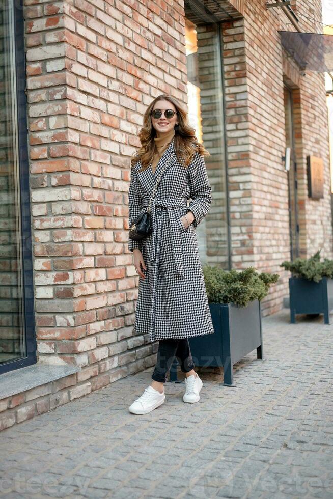 aantrekkelijk meisje in een jas in de straat in een stad, zon is schijnend foto