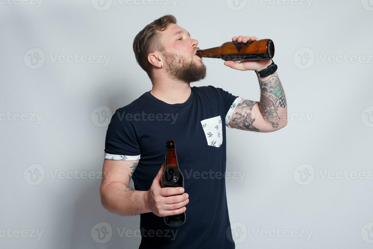 brutaal gebaard mannetje met getatoeëerd arm drankjes een bier van een fles. foto